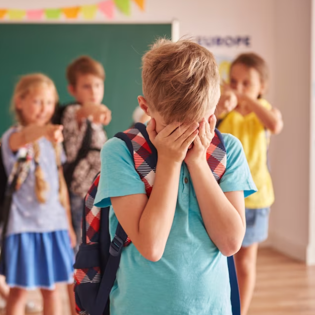 Ein Junge deckt sein Gesicht ab, während andere Kinder auf ihn zeigen.