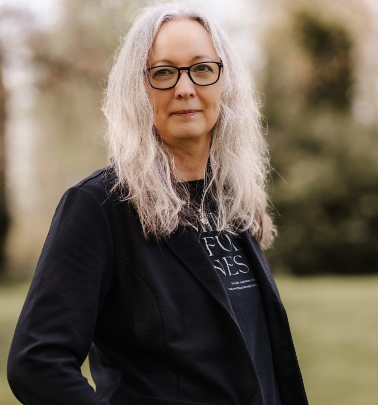 Anett Bartelt Hypnosetherapeutin Frau lächelt vor grünem, blättrigem Hintergrund.